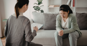 | Nashville Mental Health Therapist writes on a clipboard while client sits on a sofa during a therapy session in a living room setting.