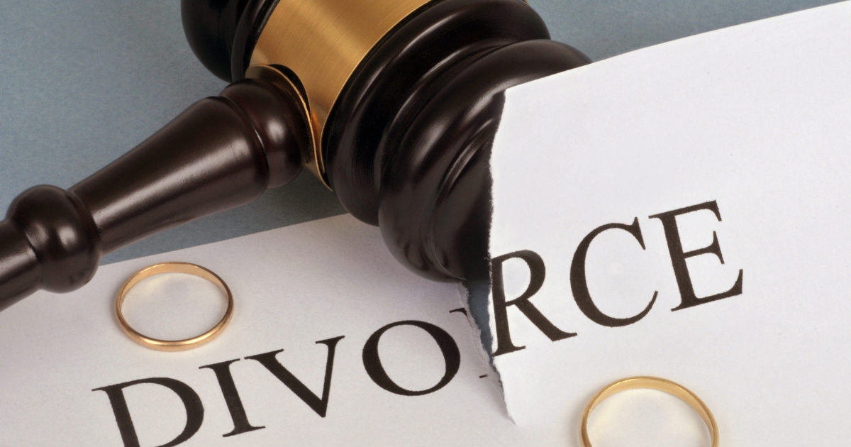 Gavel and two wedding rings on a torn divorce document, symbolizing legal separation.