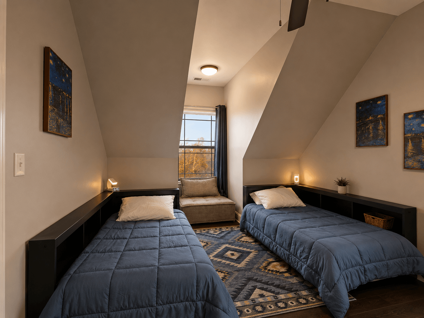 Twin bedroom in an attic with two single beds in blue quilts, dark low shelves and a central window nook. It’s warmly lit with wall lamps and a rug on the floor.