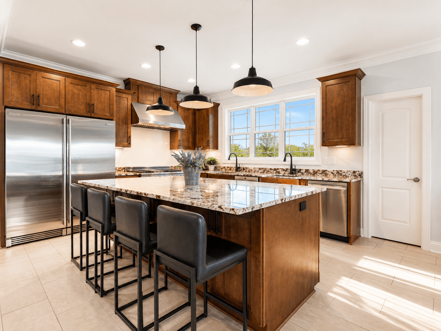 Bright kitchen with granite island, dark wood cabinets, stainless steel fridge, and a double sink by a large window.
