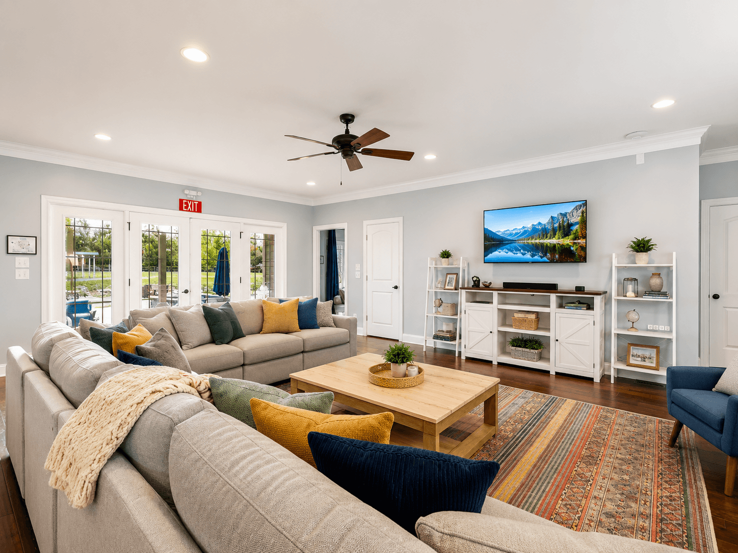 Spacious living room with a beige sectional, colorful cushions, a light wood coffee table, and a wall-mounted TV above a white cabinet.