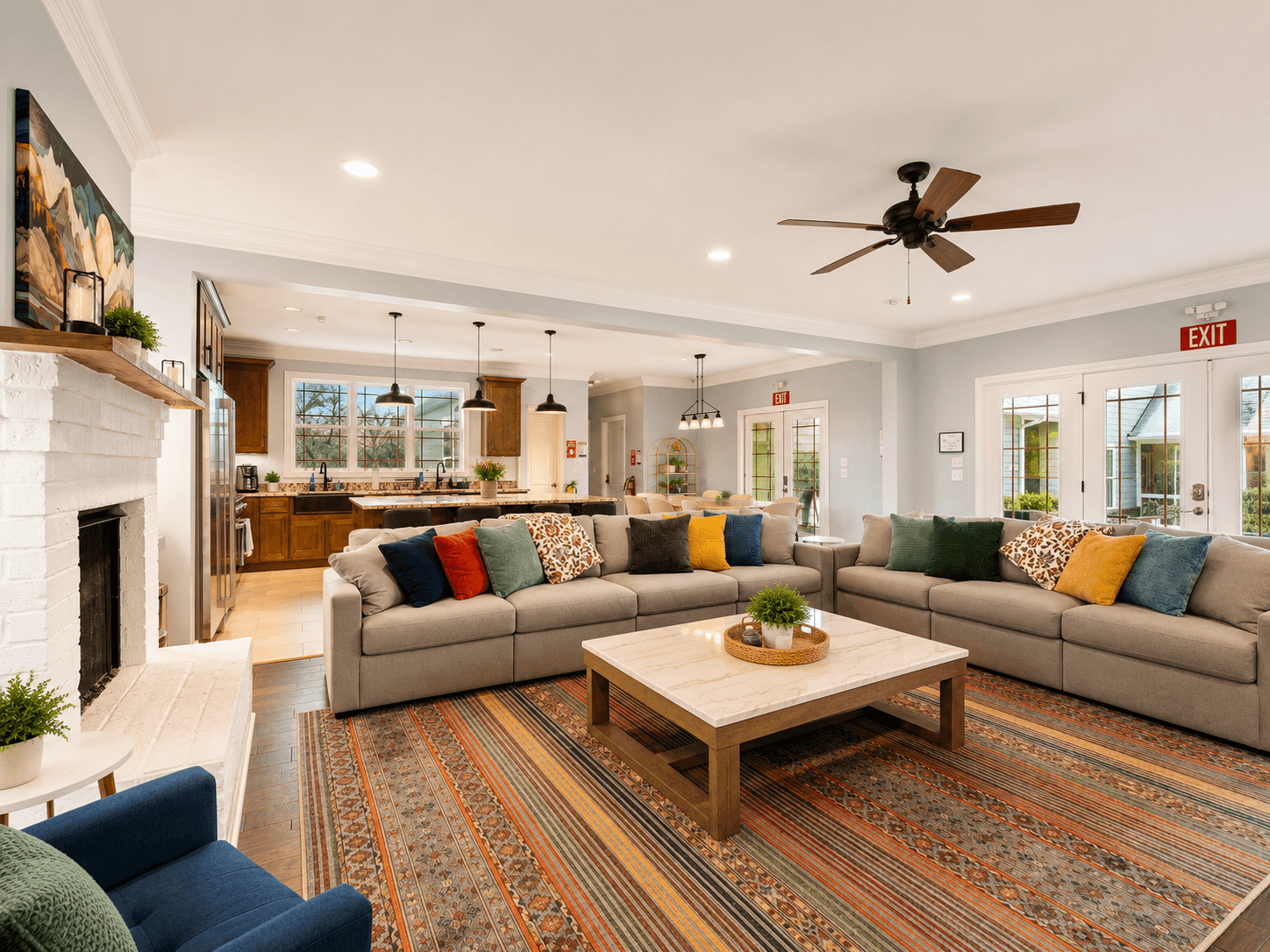 Open-concept living room with a large gray sectional, colorful throw pillows, and a marble-topped coffee table on a patterned rug.