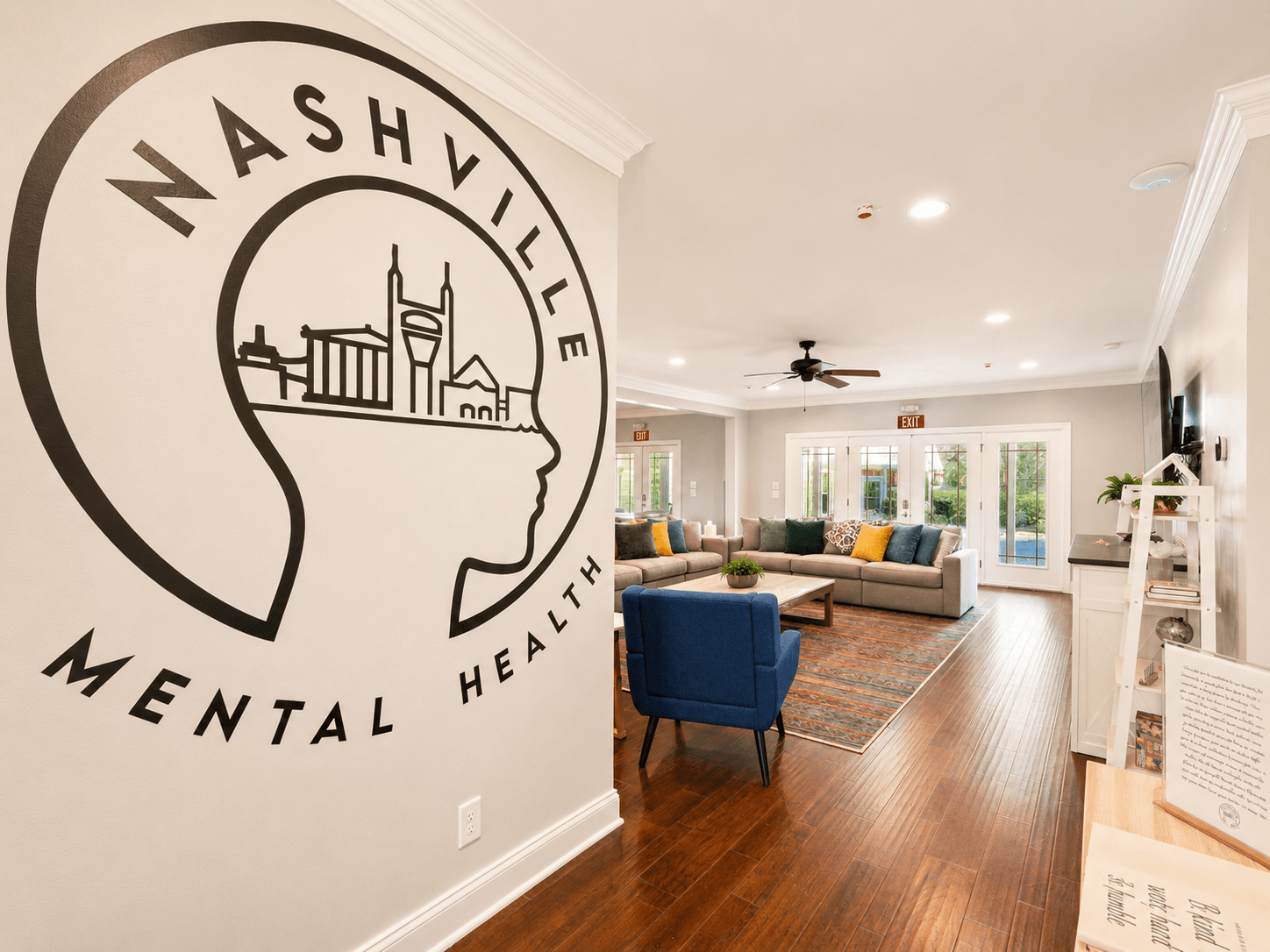 Lobby scene at Nashville Mental Health with a large wall logo of a head and city skyline, beige walls, and a blue chair facing a sofa array.