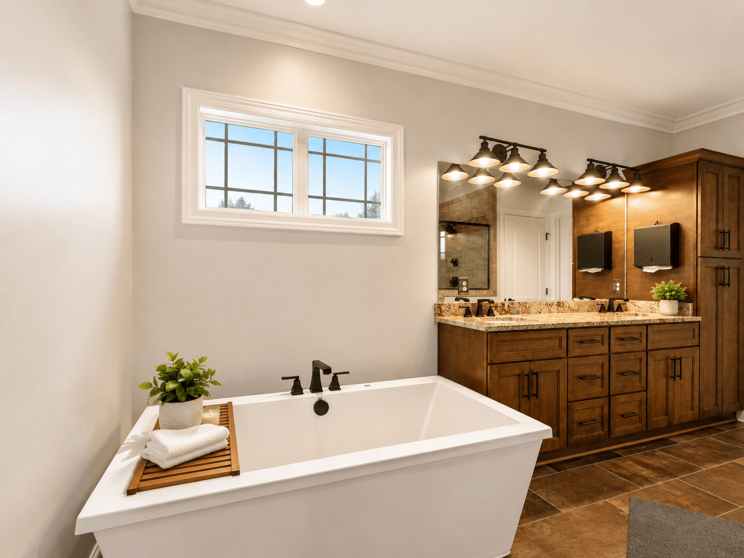 Modern bathroom with a white freestanding tub, wooden vanity, granite countertop, and a large mirror with multiple light fixtures above it.