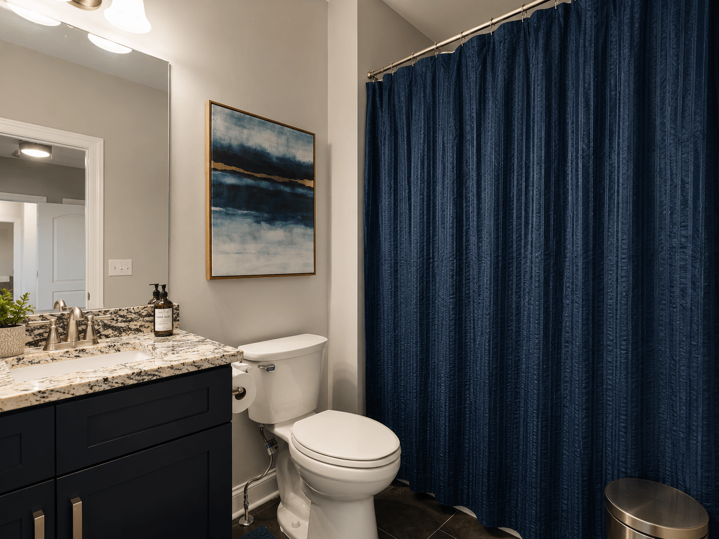 Bathroom with navy shower curtain, dark blue vanity, granite countertop, and abstract blue artwork on the wall.