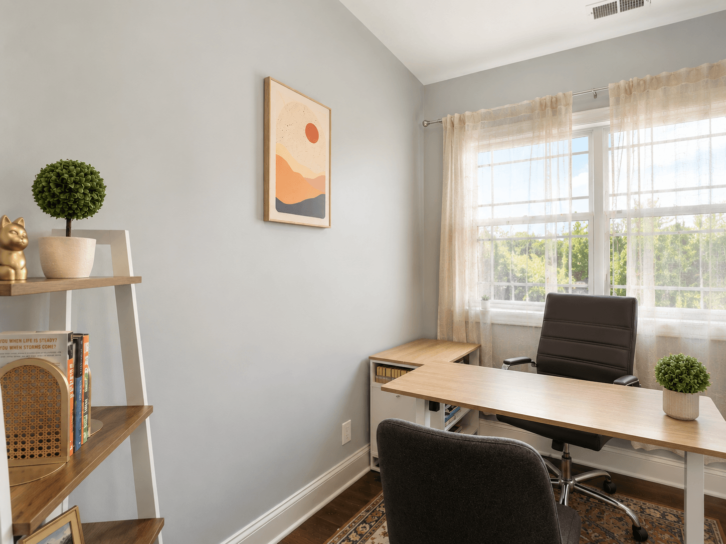 Bright home office with an L-shaped wooden desk, black leather chair, large window with sheer curtains, and potted plants on desk and shelf.