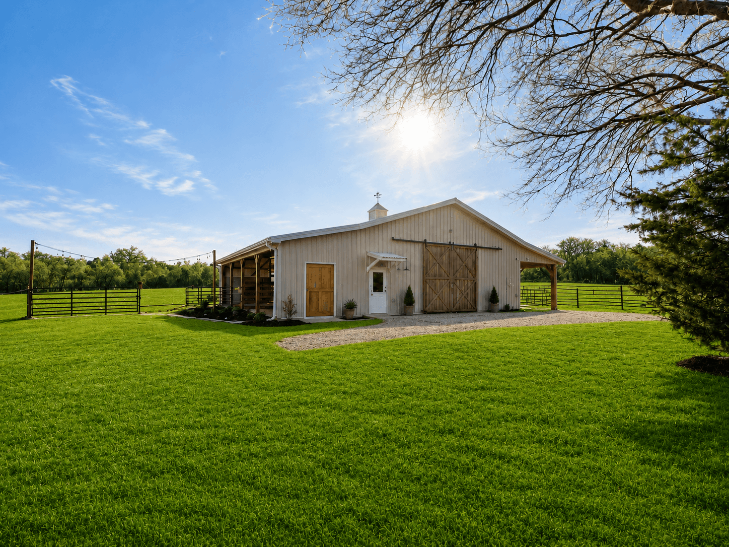 White barn with large wooden doors on a bright sunny day, green lawn and a gravel path leading to the entrance.