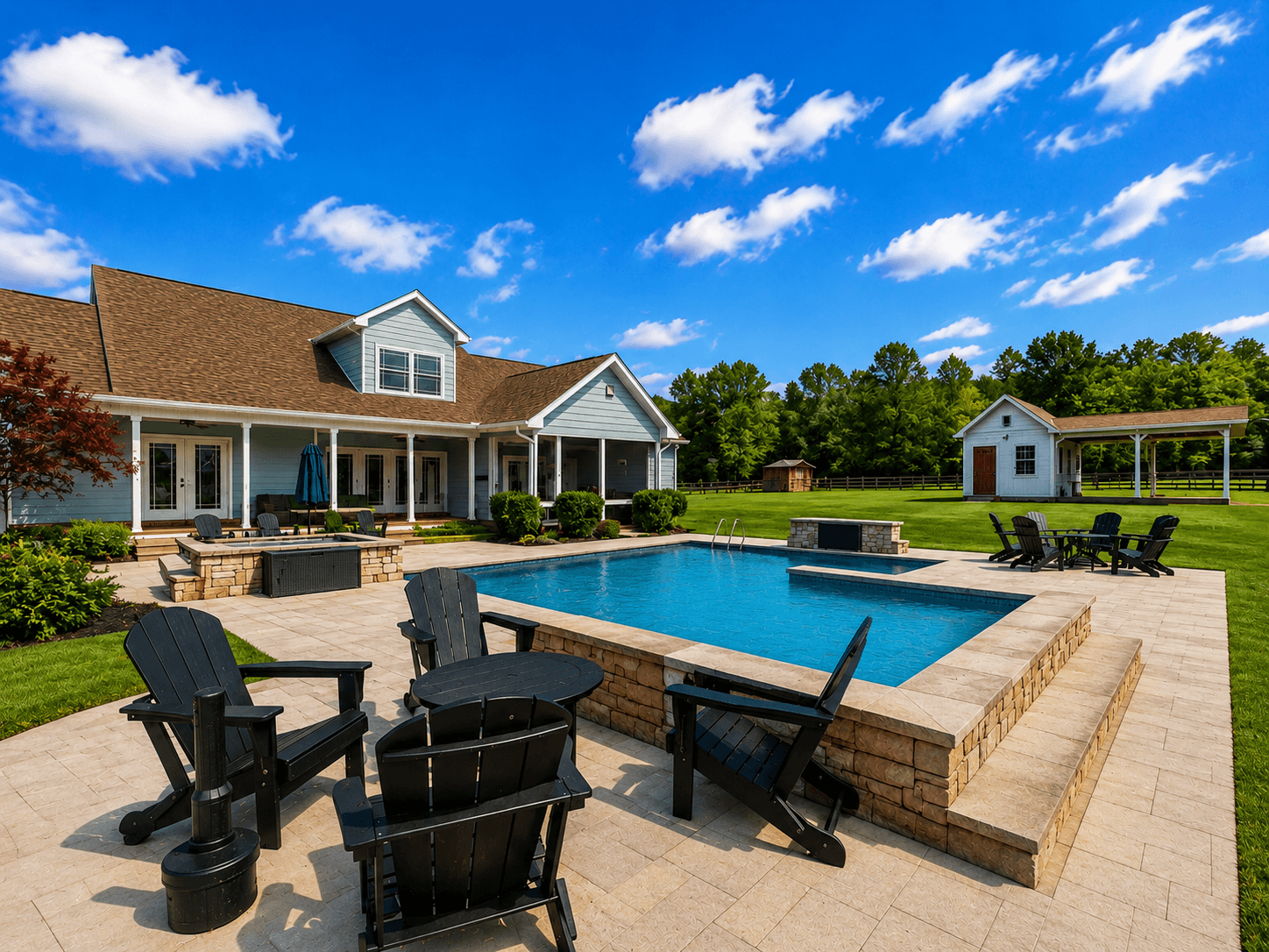 Backyard pool area with stone deck, blue rectangular pool, and black Adirondack chairs in front of a light-blue house under a sunny sky.